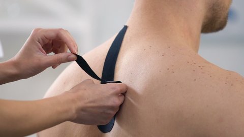 Doctor applying Y-shaped tapes on male upper back, reduce muscle tension