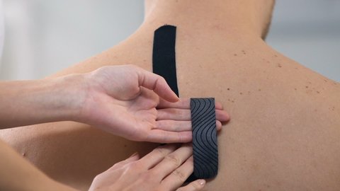 Physical therapist applying Y-shaped tapes on male upper back, muscle pain