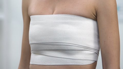 Woman in chest compression wrap touching chest, mammoplasty surgery result