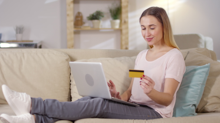 Medium shot of young Caucasian woman relaxing on sofa at home and shopping online using laptop computer and credit card | Shutterstock HD Video #1030170248