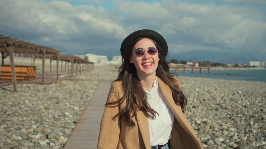 Outdoor lifestyle portrait of a cheerful and excited young brunnete girl taking off her fedora hat while walking and feeling cool wind. Smiling young adult on a joyful stroll.
