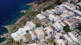 Aerial drone video of picturesque whitewashed steep cliff church of Panagia Pantanassa in main village of Folegandros island with stunning views to deep blue Aegean sea, Cyclades, Greece