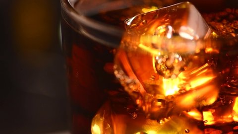 Cola with ice cubes close-up. Cola with Ice and bubbles in glass. Soda closeup. Food background. Rotate glass of Cola fizzy drink over brown background. Slow motion 4K UHD video footage