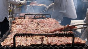 4K HD video of dozens of raw chicken breasts on skewers grilling on an open grill outside, multiple cooks turning the meat frequently while it cooks. Popular street fair cuisine.