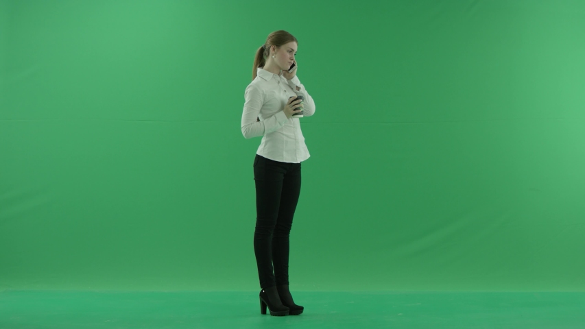 business woman is talking on her mobile cell phone with a cup of coffee or tea. She wears formal dress: white shirt and blak trousers. Businesswoman think, got idea and smile over green screen