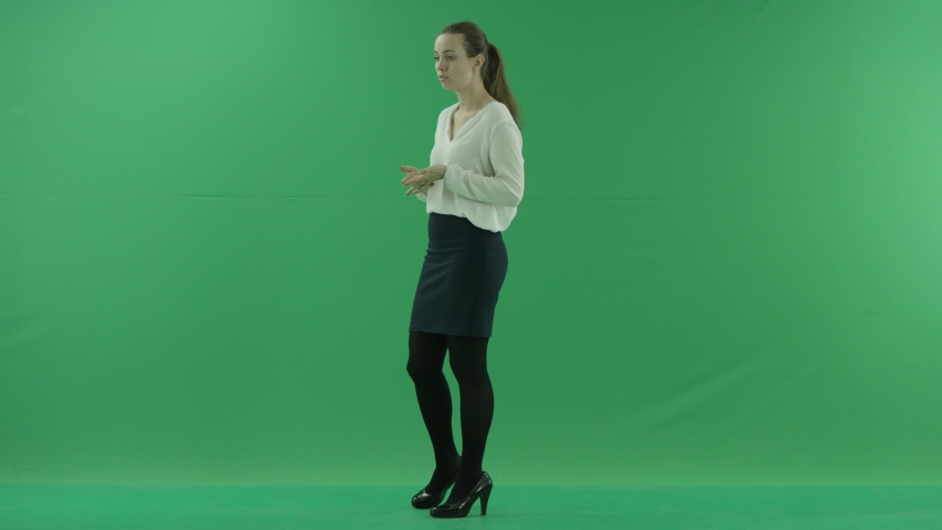 a thoughtful woman is talking, getting the idea pointing at her watch. She wears formal dress: white shirt and blak skirt. Lady stands sideways in the centre of a green screen