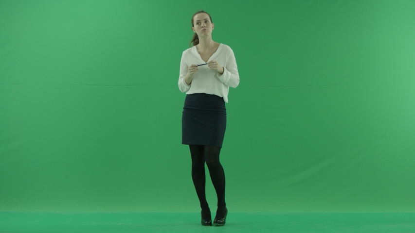 a thoughtful woman is thinkig, getting the idea grinding retractable ballpoint pen. She wears formal dress: white shirt and blak skirt. Lady stands front in the centre of a green screen