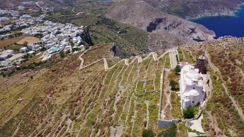 Aerial drone video of picturesque uphill church of Panagia built on a steep cliff (Virgin Mary) with stunning views to chora of Folegandros island and deep blue Aegean sea, Cyclades, Greece