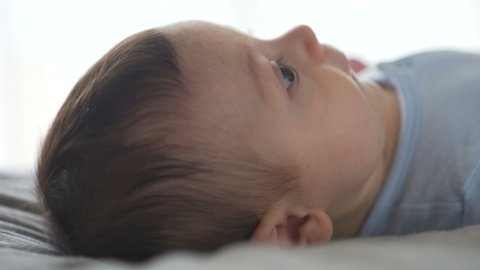Cute baby lying on the bed, looking around, smiling. Side view, close-up shot