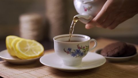 Tea being poured into tea cup. Dessert and hot drink. Lemon slices. Tea time.