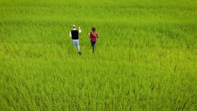 Aerial view of agronomist and young student with document in her hands writes results of observation and control of growing crops in fields. Drone shoots video about technology of agricultural food