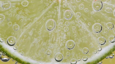 Extreme Close-Up Green limes slice cold cocktail, lime refreshing with soda sparkling water bubbles.