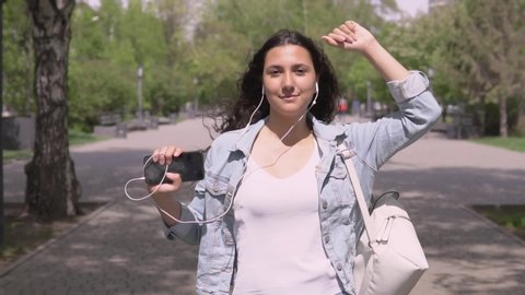 funny girl with long hair walks down the street and dances listening to music on headphones.slow motion
