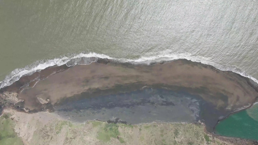 A descending fast paced video down on a beach as the waves are closing it around. 4k video speeded up