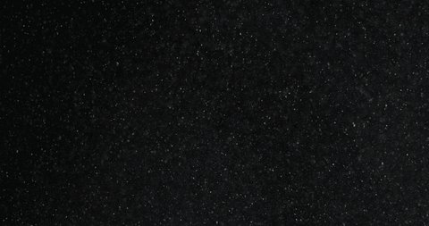 White dust particles ascending slowly in front and floating in space on black background