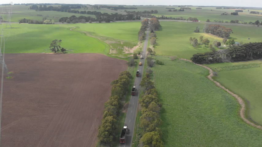 Distant aerial following farming vehicles along long straight road.