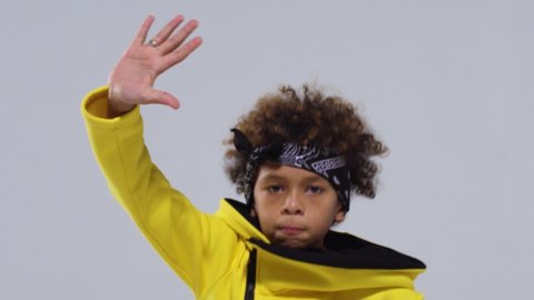 black guy with curly hair and a headband, hoodie dances, expresses emotions and waves his hands like a rapper on a gray background. Close up