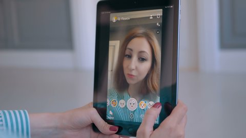 MOSCOW, RUSSIA - MAY 15, 2019: Woman using Snapchat multimedia messaging app with 3d face mask filter on tablet at home. Face detection technology, AR, gender change, selfie, entertainment concept