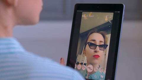 MOSCOW, RUSSIA - MAY 15, 2019: Woman using Snapchat multimedia messaging app with 3d face mask filter on tablet at home. Face detection technology, AR, social media, selfie, entertainment concept