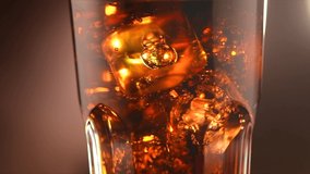 Cola with ice cubes close-up. Cola with Ice and bubbles in glass. Coke Soda closeup. Food background. Rotating glass of Cola fizzy drink over brown background. Slow motion 4K UHD video footage