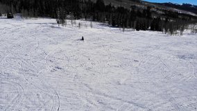 Drone Shot Tracking A Man Riding Snowmobiling In The Snowy Forest In The Winter. Aerial video showing a man driving fast motor sled in the snowy lawn.