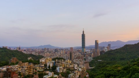 Beautiful aerial time lapse view of Taipei city skyline during night to day from afar with Taipei 101 surrounded green mountains in Taiwan. Sunrise to day. Zoom out motion timelapse.
