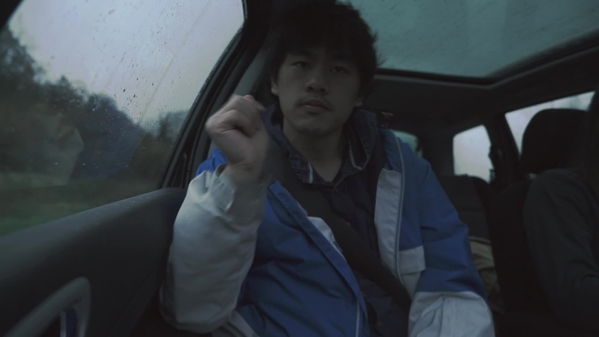 A male passenger looks out the window of a moving car, forest landscape