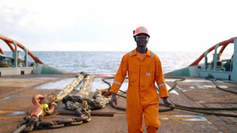 Seaman AB or Bosun walking on deck of vessel or ship , wearing PPE personal protective equipment - helmet, coverall, lifejacket, goggles. Safety at sea
