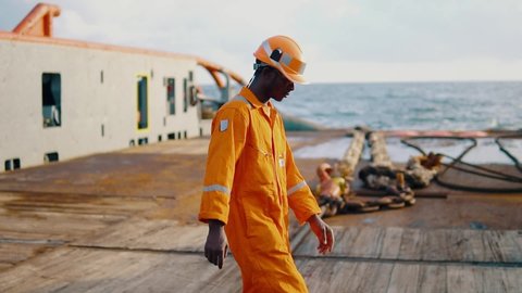 Seaman AB or Bosun walking on deck of vessel or ship , wearing PPE personal protective equipment - helmet, coverall, lifejacket, goggles. Safety at sea