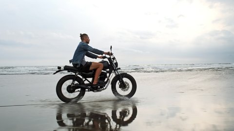 Man in riding motorcycle on beach. vintage motorbike on beach sunset on Bali. Young hipster male enjoying freedom and active lifestyle. Adventure travel concept.