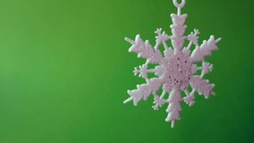 Christmas background, seamless looped video: close-up of white shiny snowflake (Christmas decoration) on green screen background