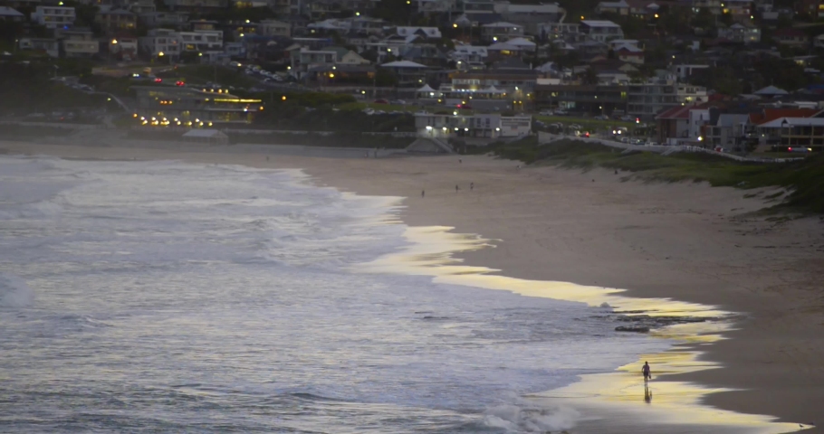 Man walking alone down the beach during Sunset at Bar Beach, Newcastle, NSW, Australia