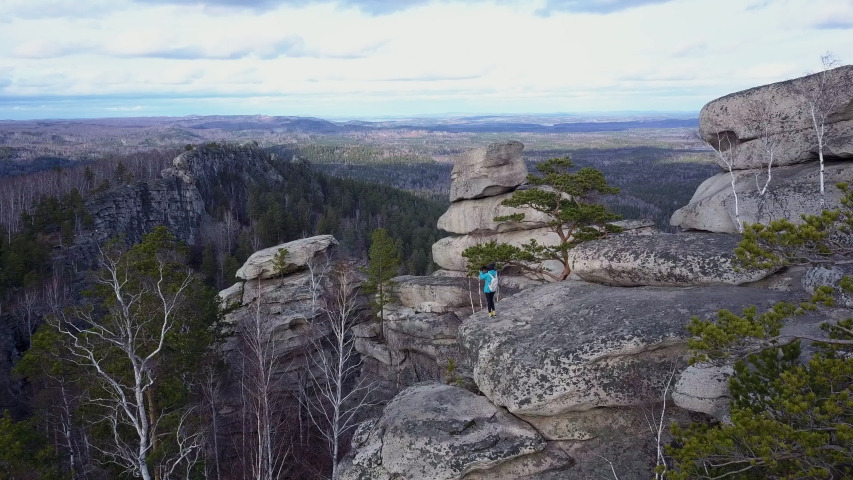 A young brave girl enjoying of view to autumn colored terrain staying on the dangerous huge stones; cold weather of late autumn and scenic cloudscape; beautiful pine tree growing between rocks, Aracul