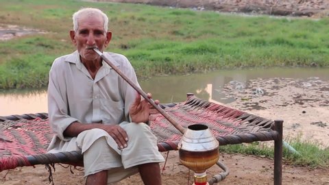 Faisalabad, PAKISTAN - An unidentifiable old man smoking shisha also called hookah in a countryside. There are about 24 million smokers in Pakistan.