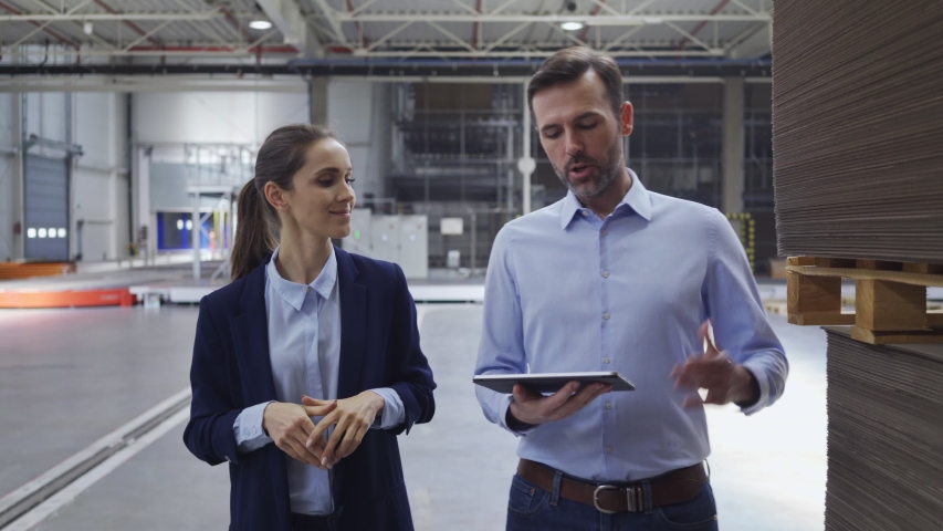 Two factory floor managers discussing work while walking and looking at tablet