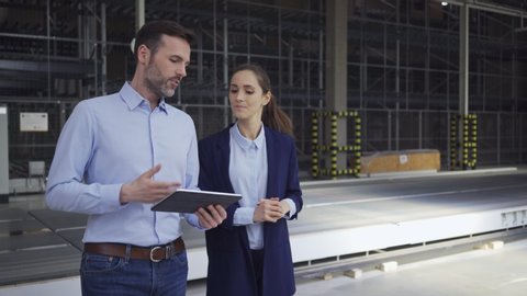 Two engineers looking at tablet and talking while walking in factory hall