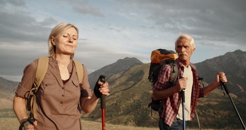 Old caucasian couple hiking, trekking in mountains with backpacks, enjoying their adventure - tourism concept 4k