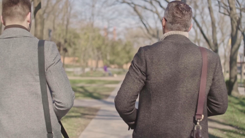 Two adult men speaking while walking in the park