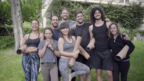 Yoga group smiling at camera outdoor. Cheerful men and women in sportswear holding yoga mats and looking at camera while standing together in park. Yoga concept