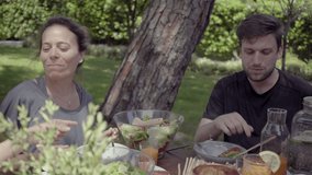 Young people eating healthy dishes in backyard. Happy male and female friends gathering around table with organic food outdoor. Healthy food concept