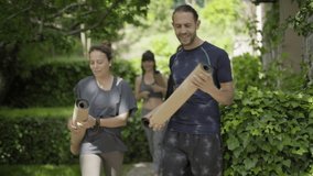 People with yoga mats walking in park. Smiling sporty people holding yoga mats and greeting each other outdoor. Yoga concept