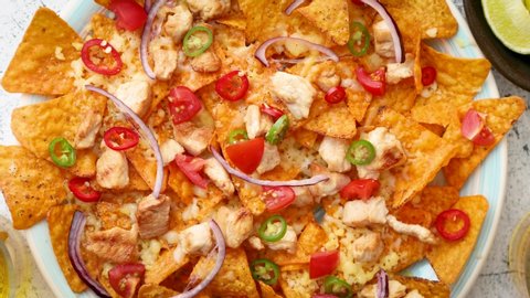 A plate of delicious tortilla nachos with melted cheese sauce, grilled chicken, jalapeno peppers, red onion, tomato, guacamole dip and spicy salsa. With cold sparkling beer.