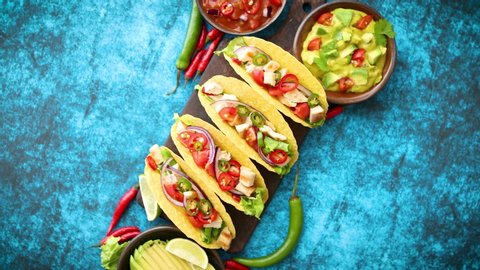 Mexican taco with chicken meat, jalapeno, fresh vegetables served with guacamole and tomato salsa. Latin american food. Placed on blue table.
