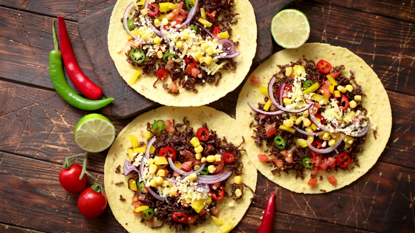 Healthy corn tortillas with grilled beef, fresh hot peppers, cheese, tomatoes over rusty wooden table background, top view, copy space. Mexican food contept.