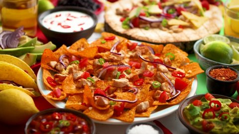 An overhead photo of an assortment of many different Mexican foods, including tacos, guacamole, nachos with grilled chicken, tortillas, salsas and others