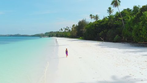 Aerial slow motion: Woman walking on white sand beach turquoise water tropical coastline Pasir Panjang Kei Islands Indonesia Moluccas Maluku Indonesia scenic travel destination