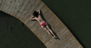 Aerial drone video on woman in swimsuit sunbathing on the pier. Female relaxing on vacations