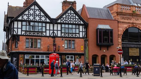 Chester, Cheshire / United Kingdom - May 25 2019: Timelapse at Chester Northgate street. Dynamic flow of people rushing in beautiful street with old Tudor house and the red English telephone booth.