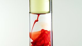 video footage of red food colr ink drop from oil into water in clear test tube, close up, full high definition resolution, thirty frame per second, slow-motion