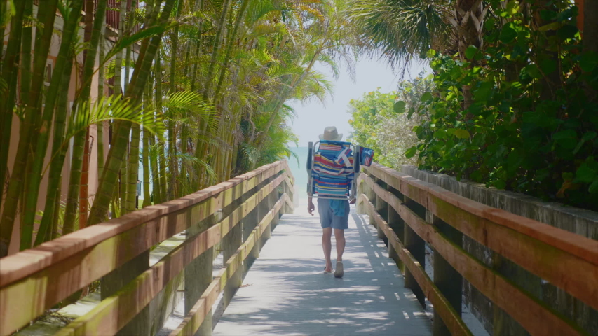Beach bum walks down pathway towards Florida beach and ocean